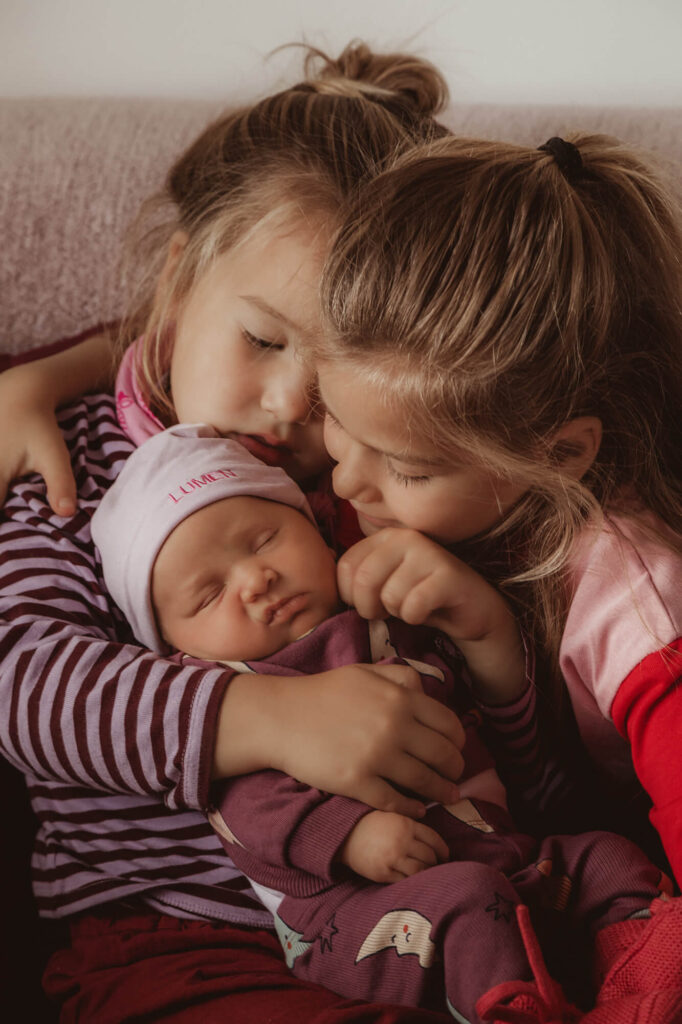Twee grote zusjes knuffelen de slapende baby op de bank