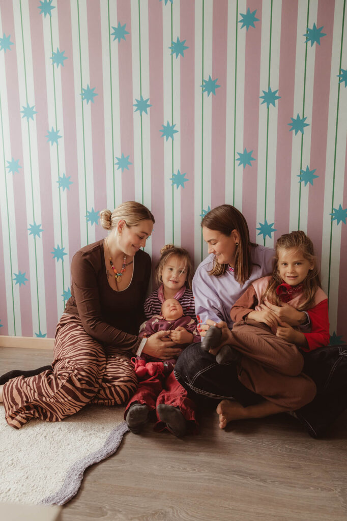 Newbornshoot thuis voorbereiden met het hele gezin: ouders en twee grote zusjes op de vloer van de babykamer
