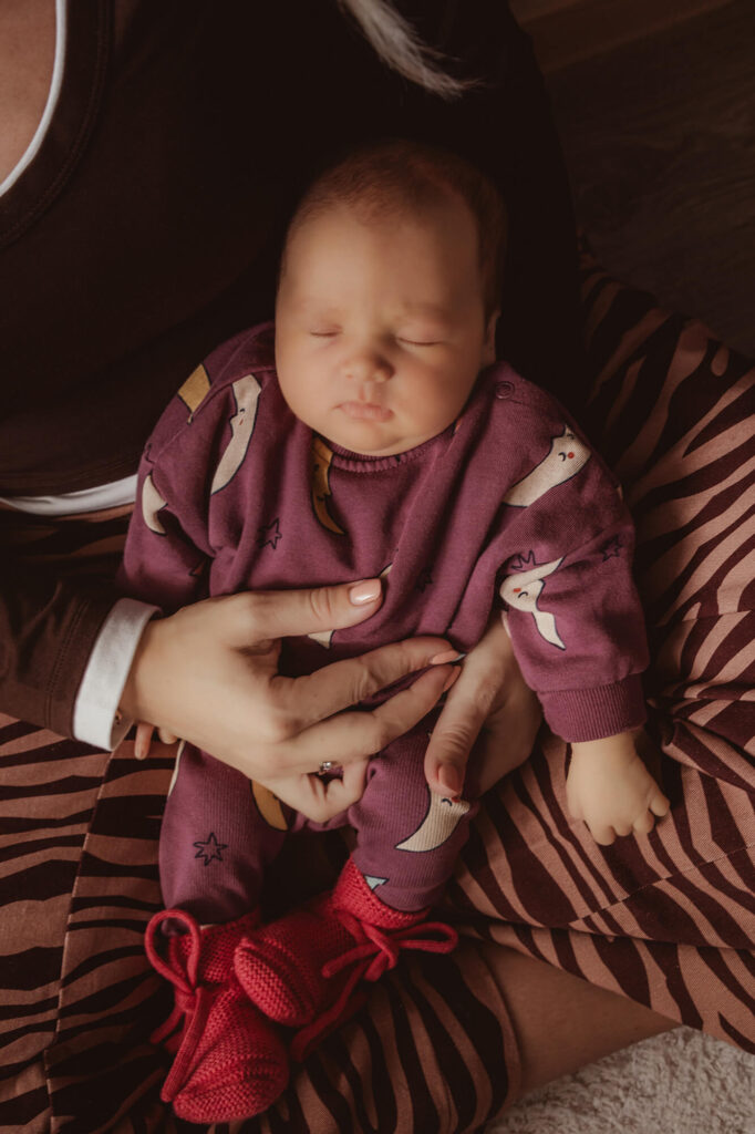 Slapende newborn met rode gebreide slofjes op schoot bij mama in een broek met zebraprint