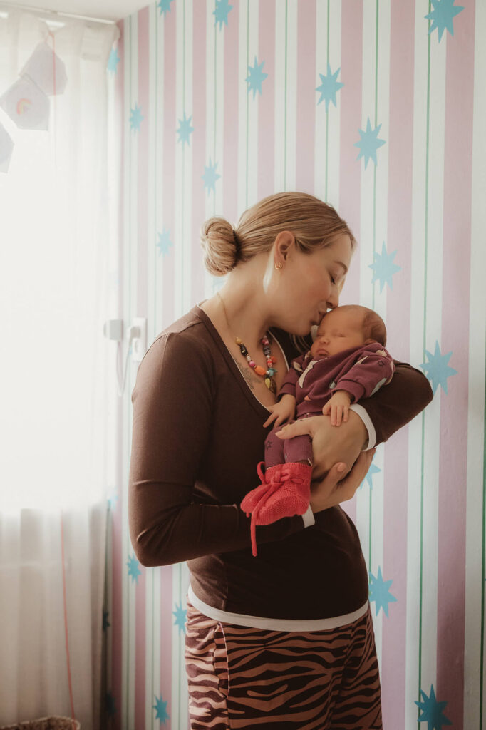 mama kust haar pasgeboren baby bij het raam in de babykamer