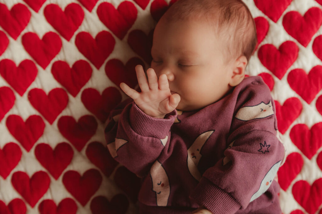 Slapende newborn met een handje bij het gezicht op een deken met rode hartjes